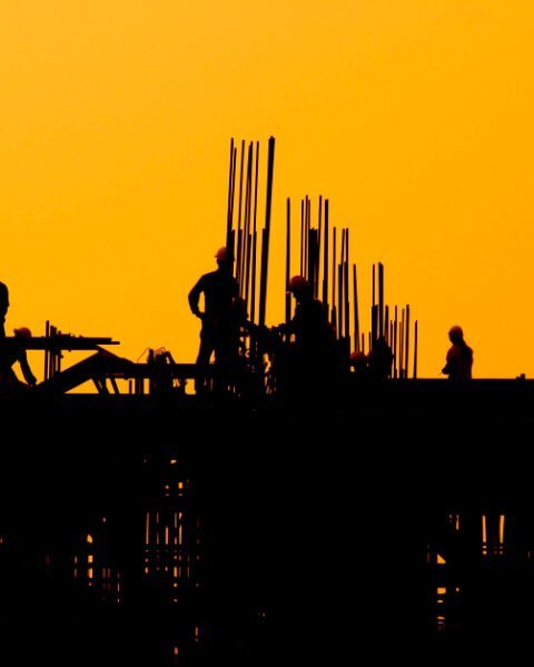 A team of workers standing together on a construction site at sunset, engaged in conversation amidst construction tools and machinery, representing Vietnam Construction Safety Standards.