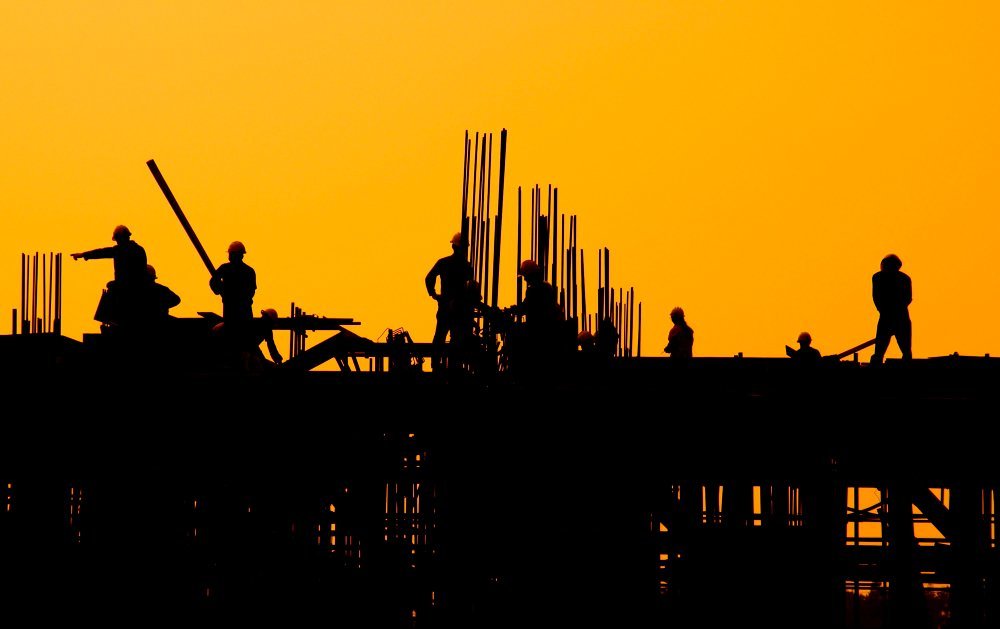 A team of workers standing together on a construction site at sunset, engaged in conversation amidst construction tools and machinery, representing Vietnam Construction Safety Standards.