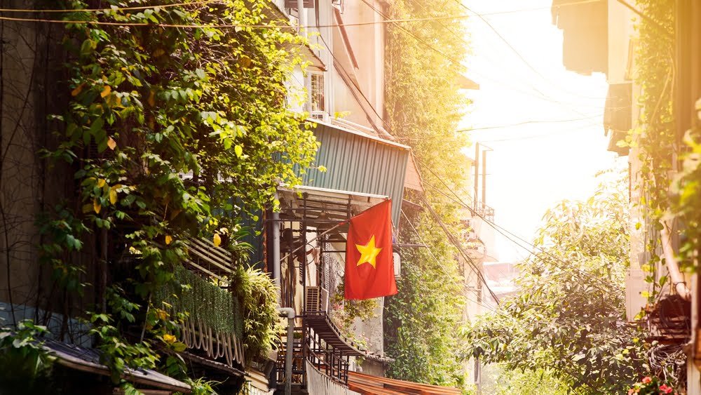 A vibrant red Vietnamese national flag waves prominently on a balcony of a house, at Hanoi city street, symbolizing national pride and unity amidst the urban environment.