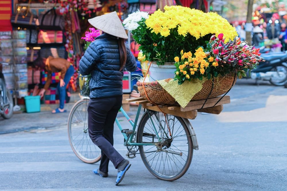 A woman pushing a bicycle loaded with vibrant flowers on a busy Vietnamese street, symbolising Vietnam Construction Labor Market.