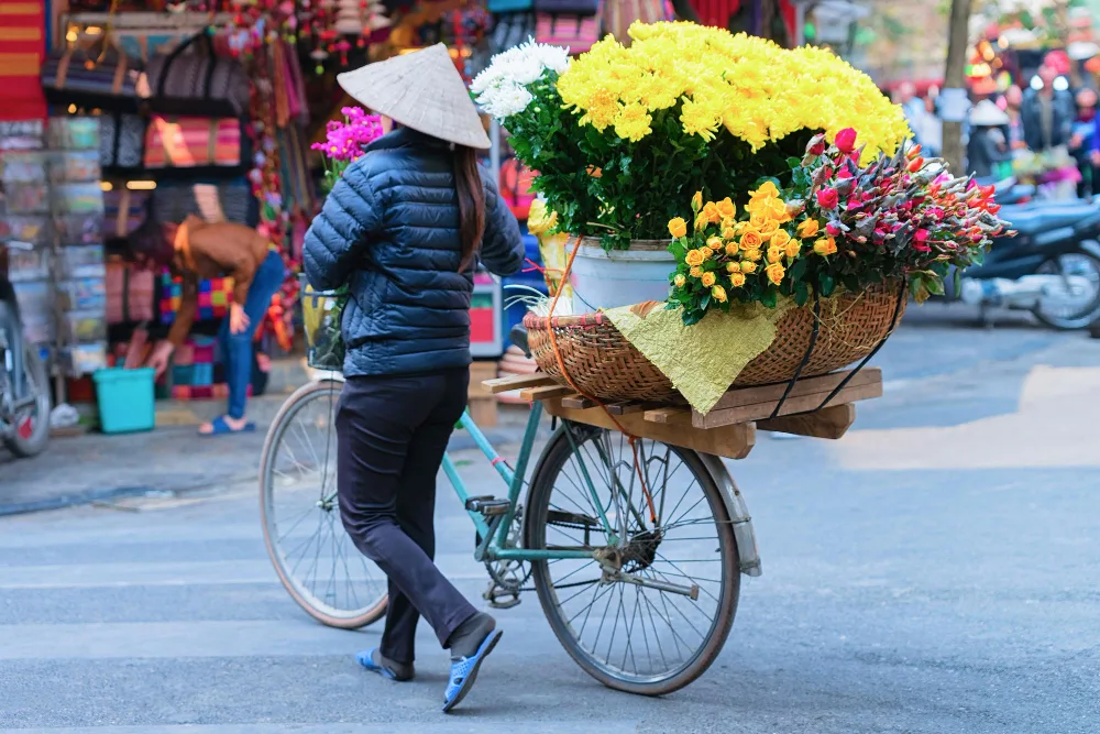 A woman pushing a bicycle loaded with vibrant flowers on a busy Vietnamese street, symbolising Vietnam Construction Labor Market.