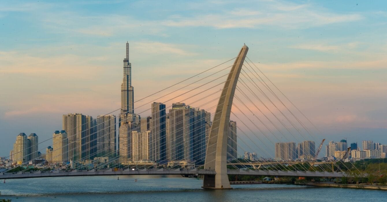 Vietnam's Public-Private Partnership: A cable-stayed bridge over a river with a city skyline and a tall skyscraper at dusk.