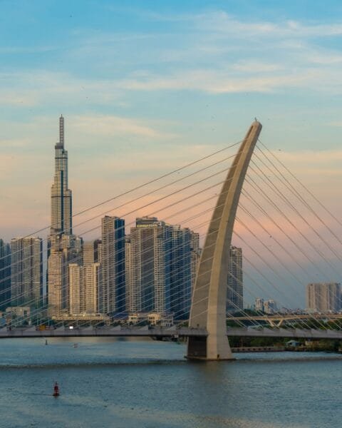 Vietnam's Public-Private Partnership: A cable-stayed bridge over a river with a city skyline and a tall skyscraper at dusk.