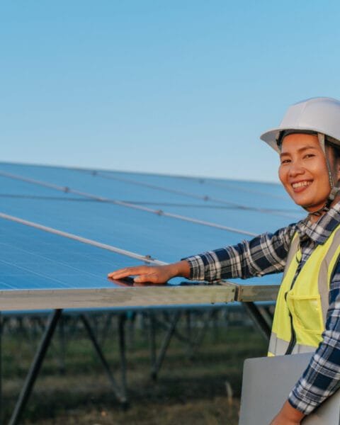 Vietnam Renewable Energy in Construction: Engineer in a hardhat and high-vis vest inspecting solar panels at sunset.