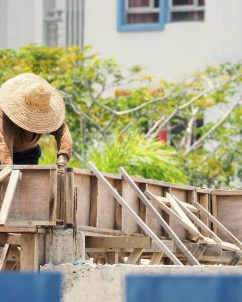 Worker in straw hat checking wooden forms for concrete at a construction site, showing Vietnam Construction Workforce Trends.